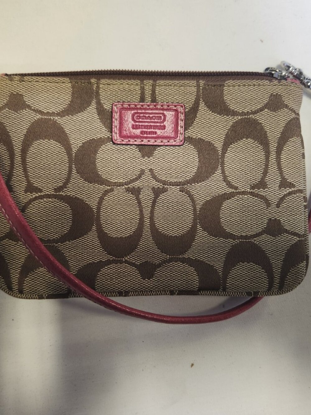 Coach monogram canvas wristlet features vibrant pink leather trim and a top zip